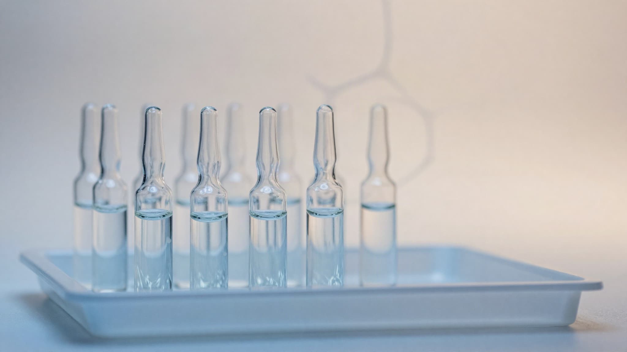 Fileira de ampolas de vidro seladas sobre uma bandeja, com uma estrutura molecular desenhada ao fundo, representando os exossomos usados em protocolos capilares